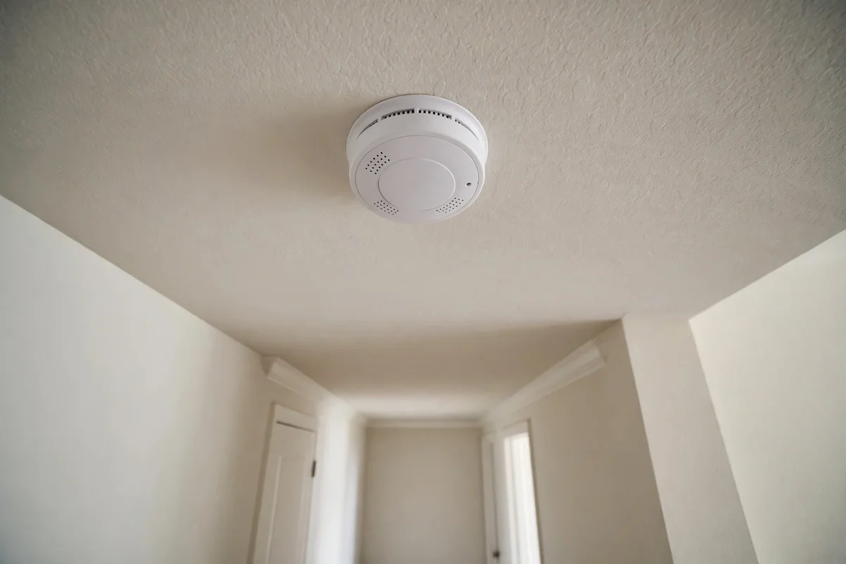 A hand pressing the test button on a hallway carbon monoxide detector